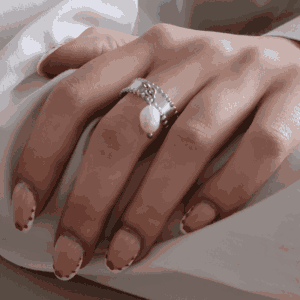 Main féminine portant une bague argenté avec une perle suspendu, bijou élégant et minimaliste en acier inoxydable