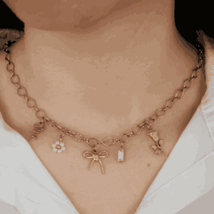 Collier doré à maillons porté autour du cou, orné de cinq charms pendentifs : une clé, une fleur perle blanche, un noeud, une pierre blanche et une tulipe, style délicat et romantique