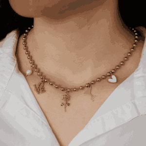 Collier doré à billes porté autour du cou, orné de cinq charms pendentifs : une perle, un love, une rose, un verre de cocktail et un cœur, style délicat et romantique