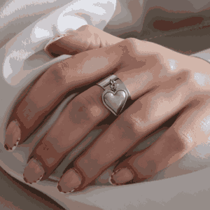 Main féminine portant une bague argenté avec cœur suspendu, bijou élégant et minimaliste en acier inoxydable