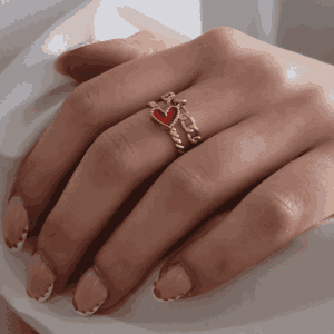 Main féminine portant une bague doré avec cœur rouge suspendu, bijou élégant et minimaliste en acier inoxydable