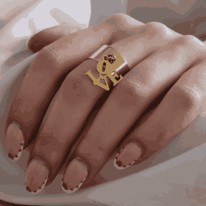 Main féminine portant une bague doré avec un love suspendu, bijou élégant et minimaliste en acier inoxydable