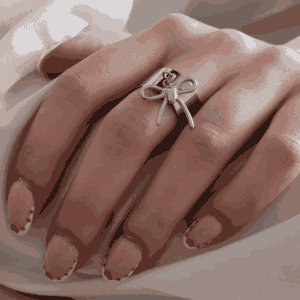 Main féminine portant une bague argenté avec nœud suspendu, bijou élégant et minimaliste en acier inoxydable