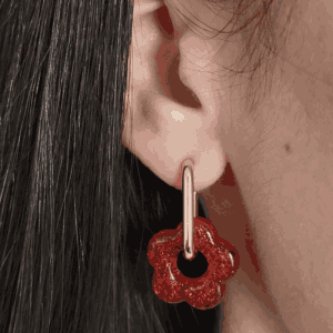 Créoles rondes doré sur une oreille feminine, orné d'une fleur rouge à paillette