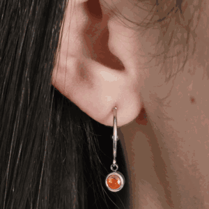 Boucles d'oreilles rondes argenté sur une oreille féminine, orné d'une pierre rouge ronde