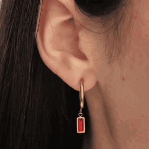 Boucles d'oreilles rondes doré sur une oreille féminine, orné d'une pierre rouge rectangulaire