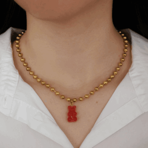 Collier doré à billes porté autour du cou, orné d'un charm pendentif : un ourson rouge, style délicat et romantique